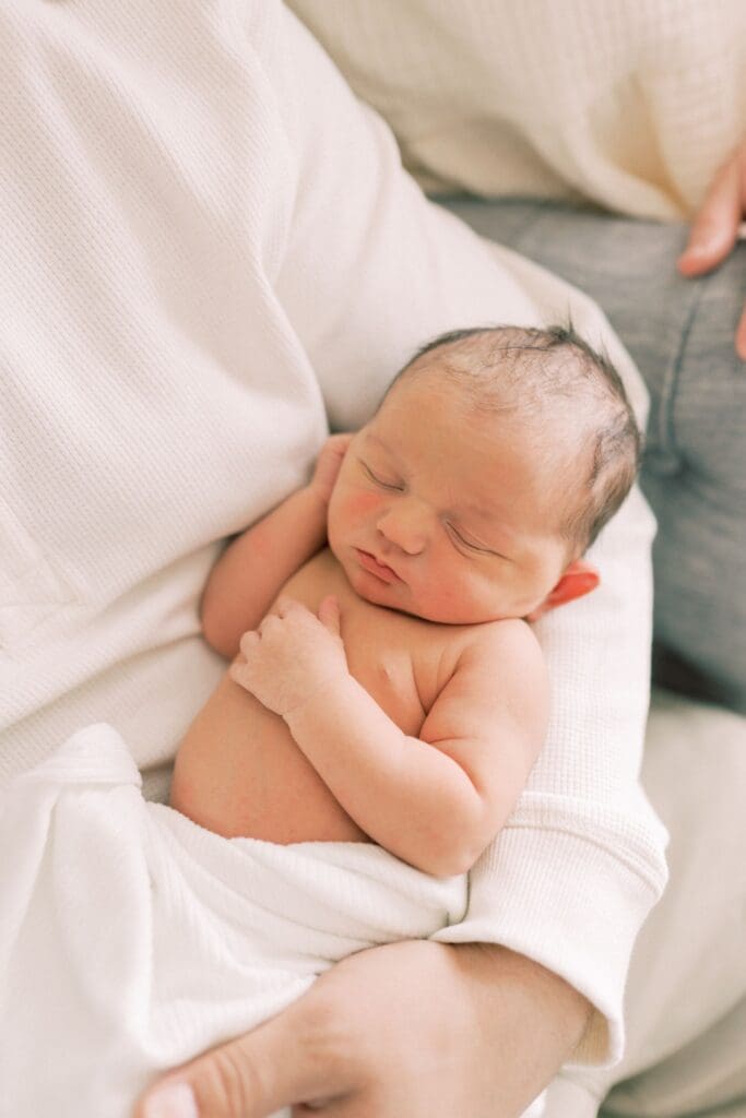 A peaceful newborn baby sleeping on soft white blankets during a gentle portrait session.